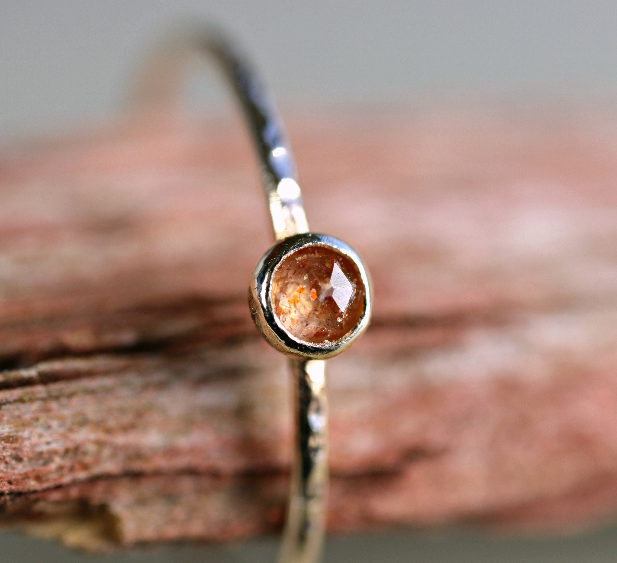 A delicate gold ring with a hammered band and a small, round, orange gemstone.