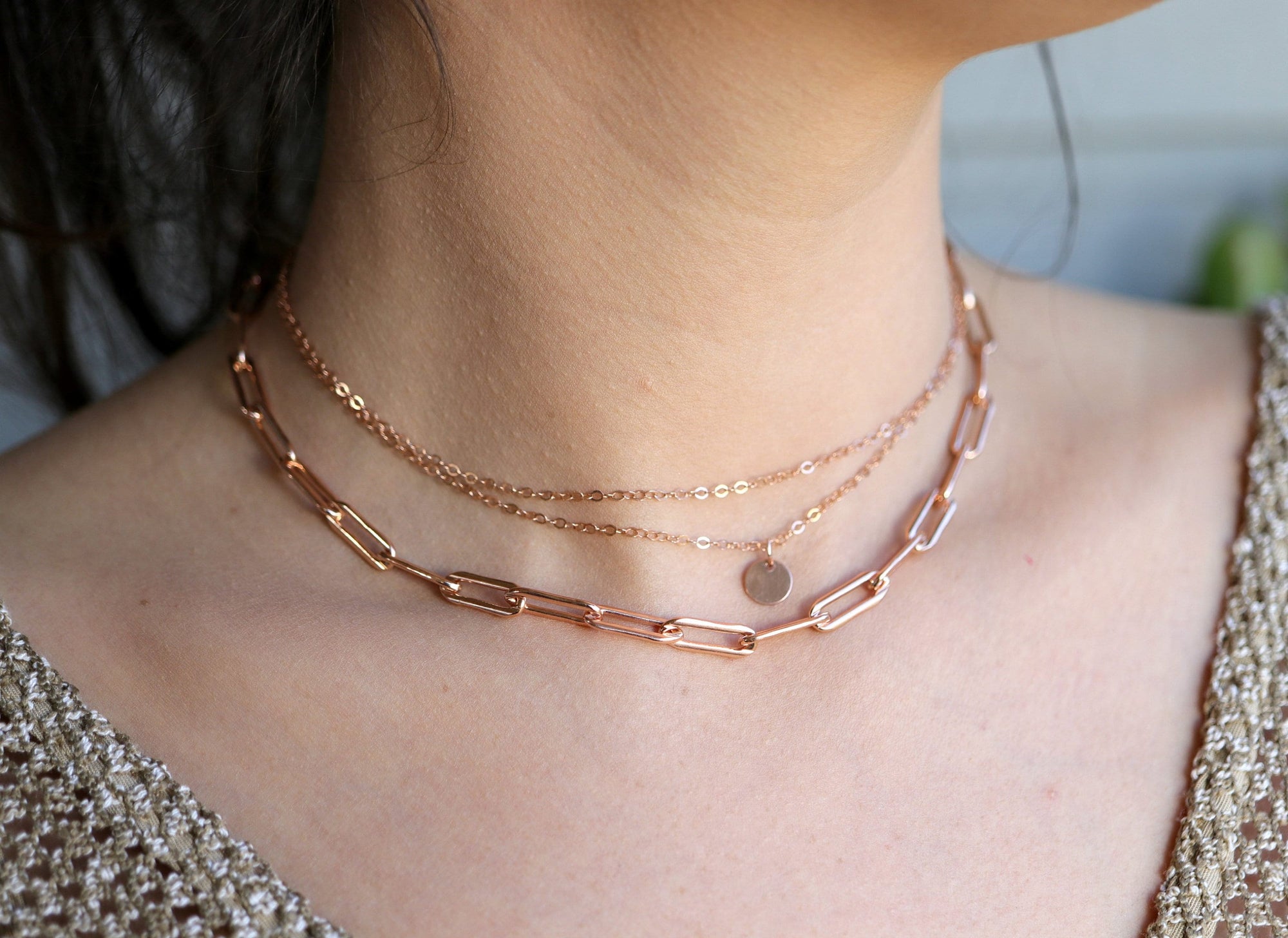 A layered rose gold necklace with a delicate chain and a larger, chunky chain with a small circular pendant.