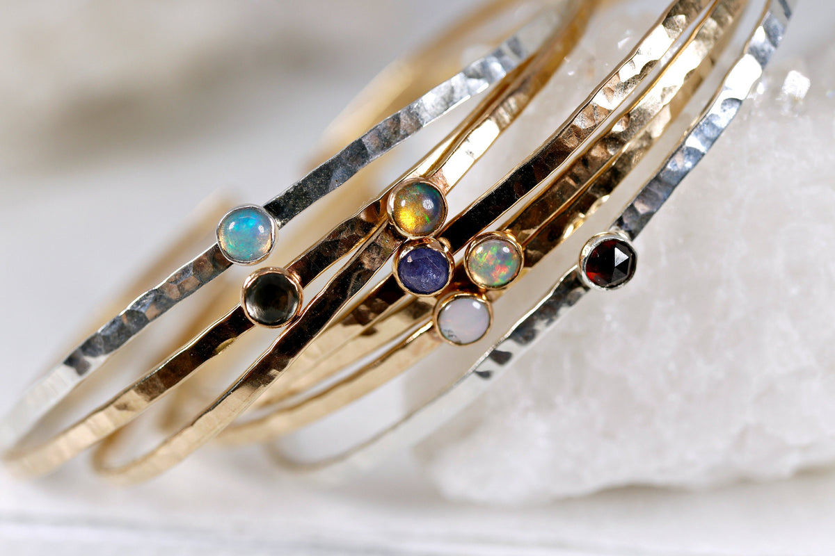 Seven gold and silver hammered stacking open cuff bracelets with various gemstones including opal, garnet, and blue topaz. Birthstone Cuff Bracelets, Gemstone Bracelet, Garnet Bangle, Moonstone Bracelet, Peridot Bracelet, Sterling Silver Cuff Birthstone Jewelry