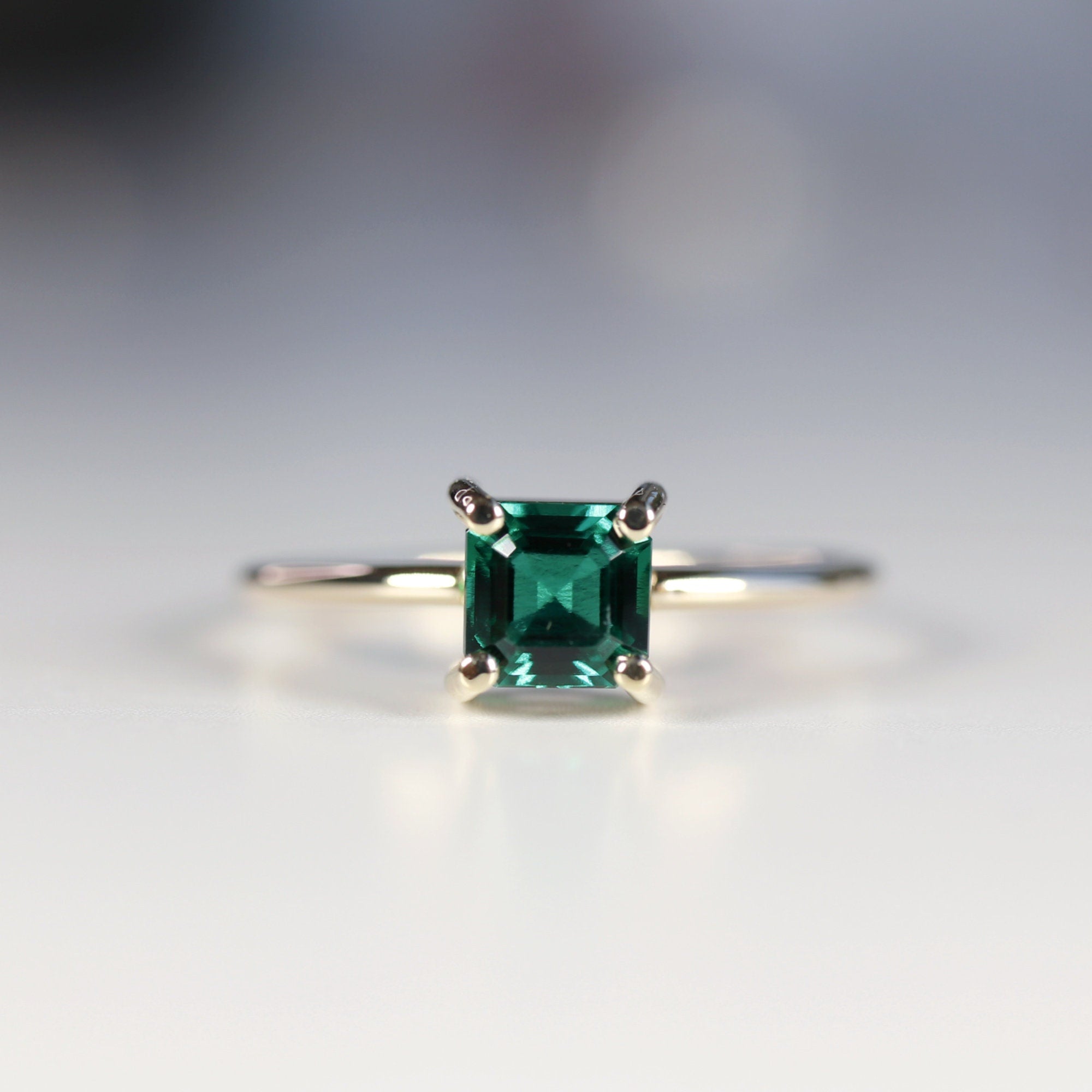 A gold ring with a square emerald green emerald gemstone set in a four-prong setting.