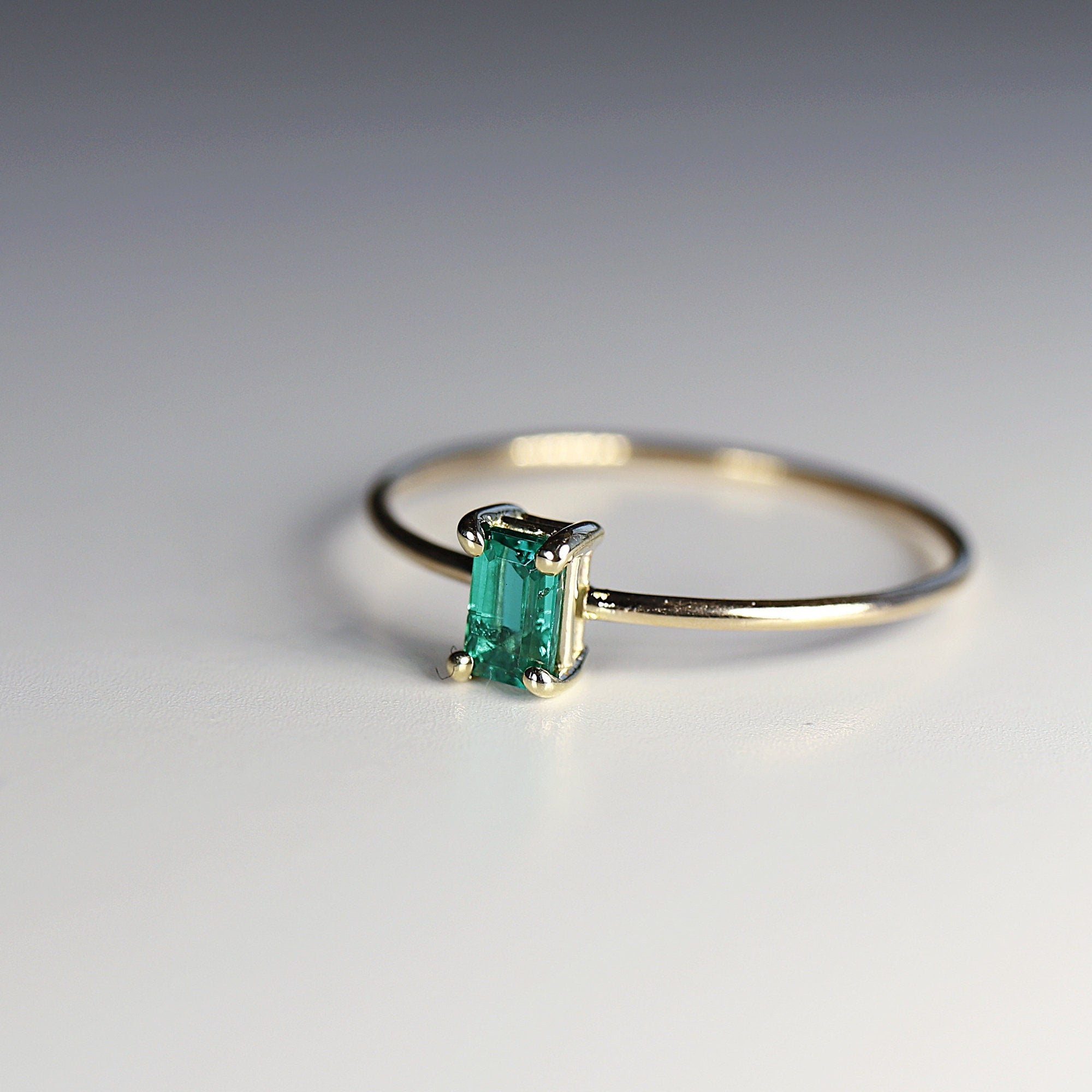 A delicate gold ring with a single emerald green gemstone set in a rectangular shape.