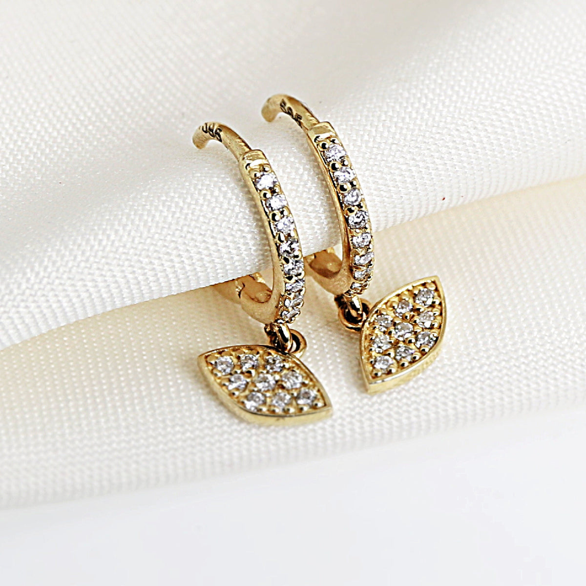 A pair of gold hoop earrings with a dangling diamond-shaped charm. The charms are set with small, clear diamonds.