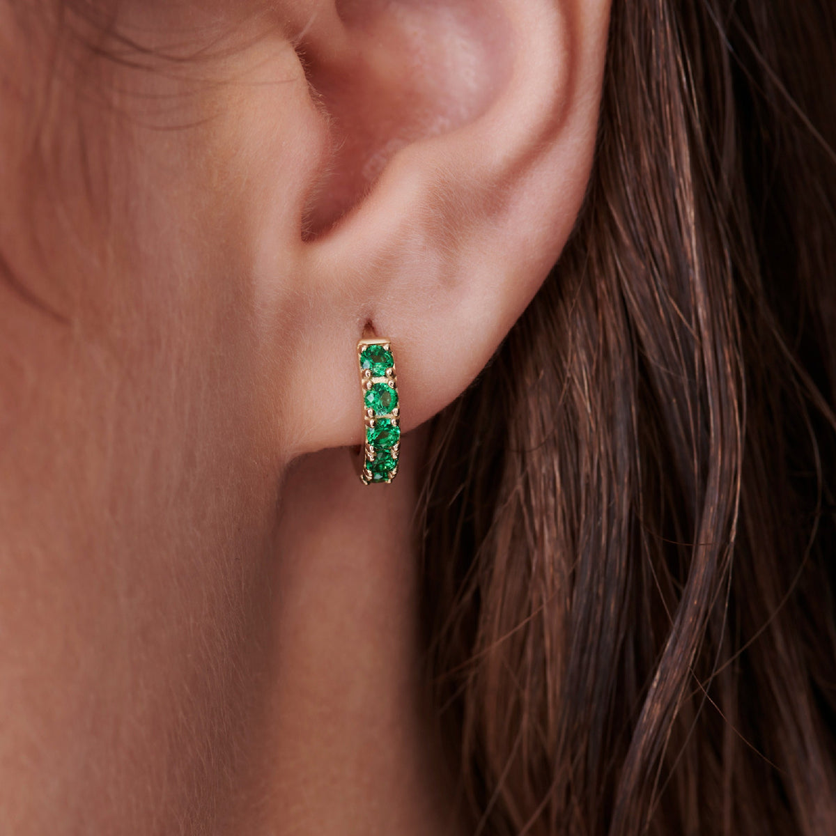 Gold hoop earrings with a row of green emerald gemstones.