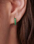 Gold hoop earrings with a row of green emerald gemstones.