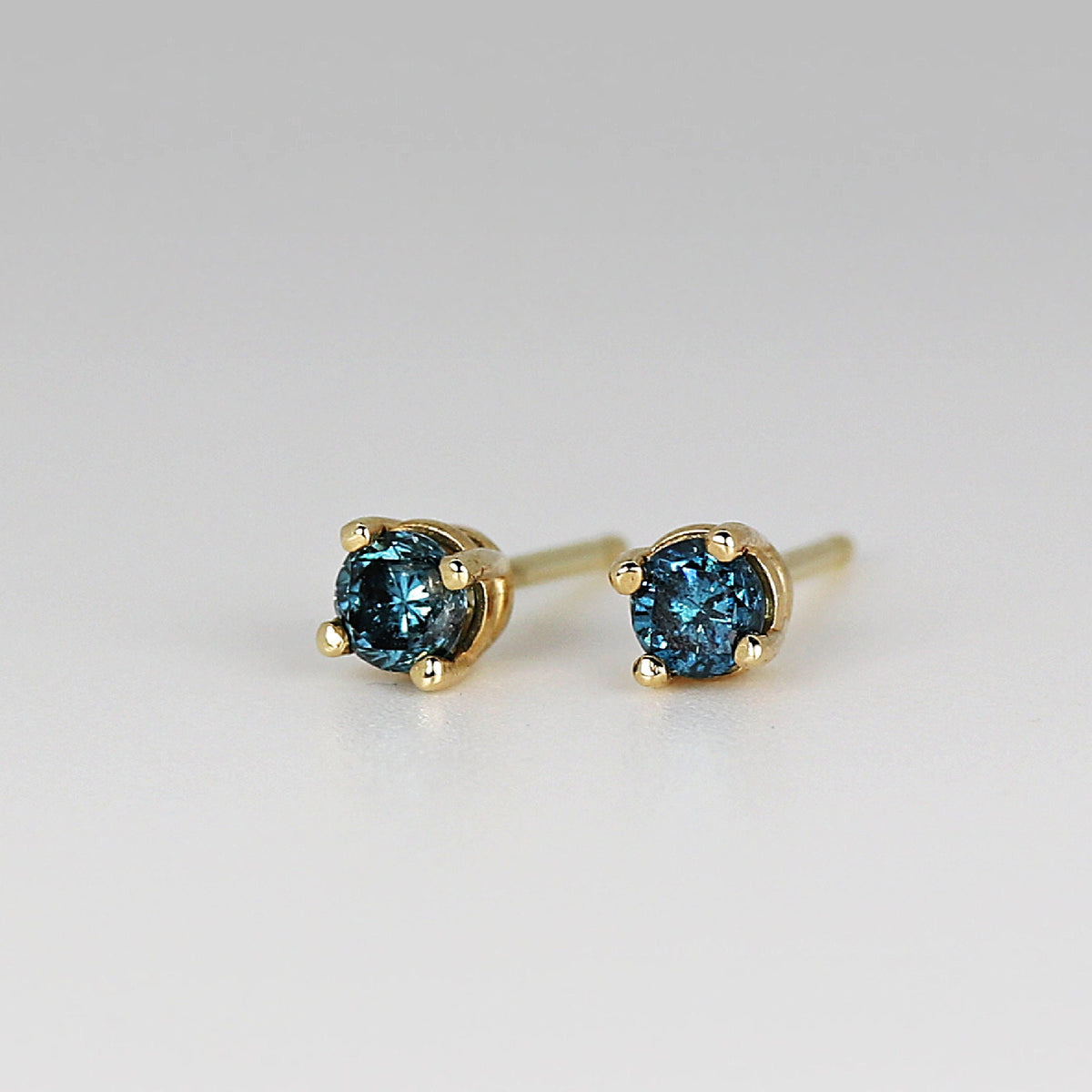 A pair of gold stud earrings with blue round sapphire gemstones.
