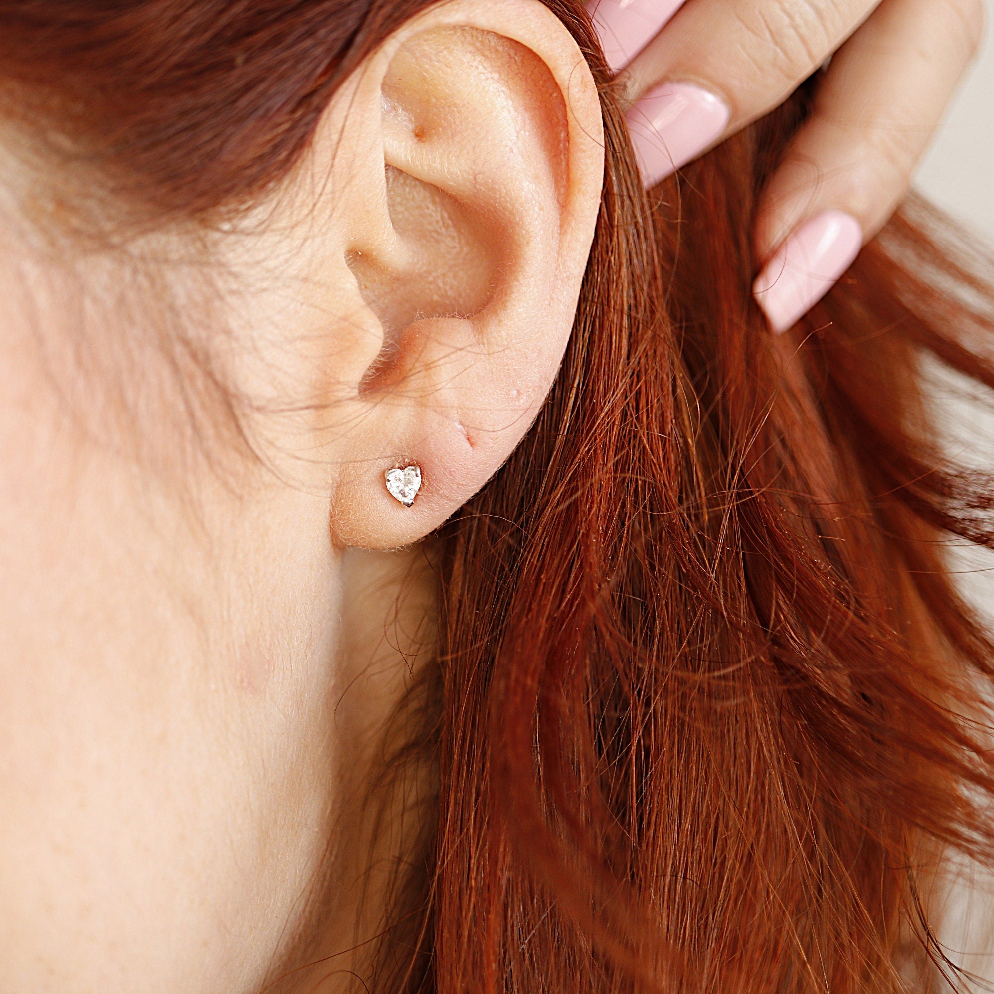 A close-up of a person's ear with a small heart-shaped diamond earring.