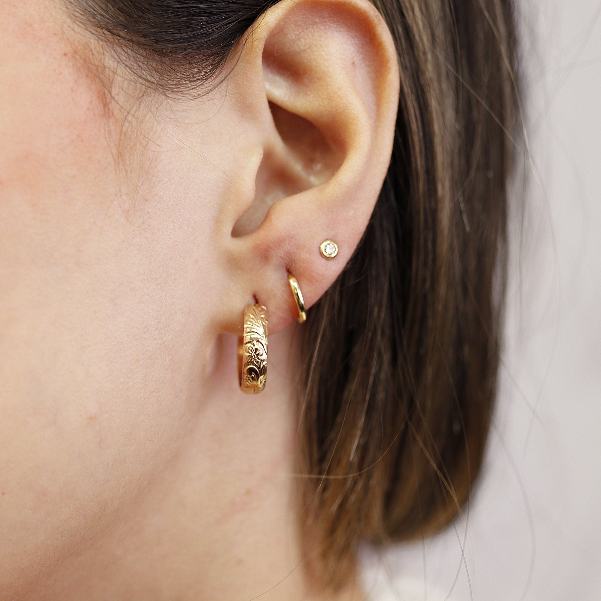 Model wearing small floral-patterned gold filled hoop earrings with a thick, open hoop design. Close-up shot showing earring size and detail.
