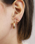 Model is wearing floral pattern small gold hoop earrings.