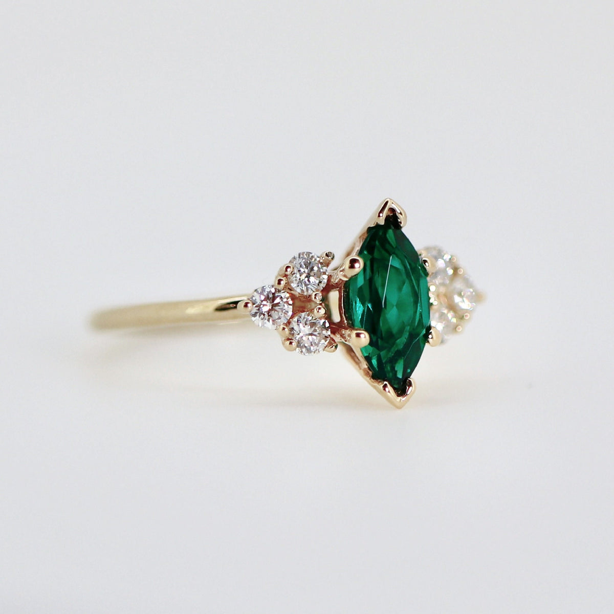 14k Gold Marquise Emerald Ring with Diamond Accents. A gold ring with a marquise-shaped emerald green gemstone surrounded by smaller clear gemstones.