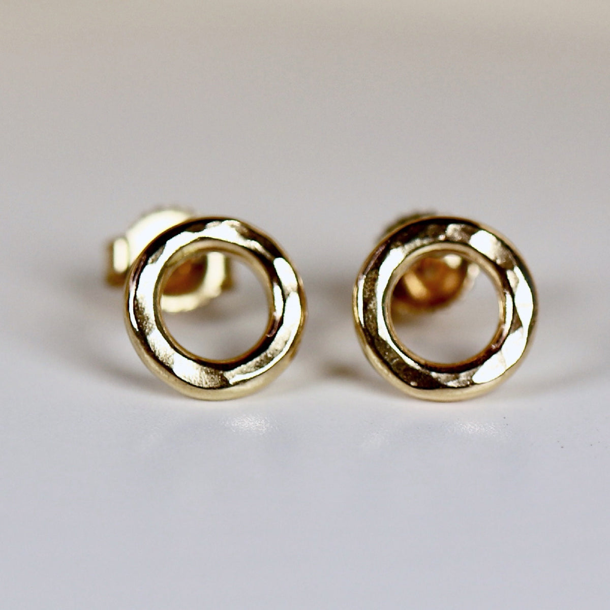 A pair of gold hammered circle stud earrings. The earrings are simple and elegant, and would make a great gift for any occasion.