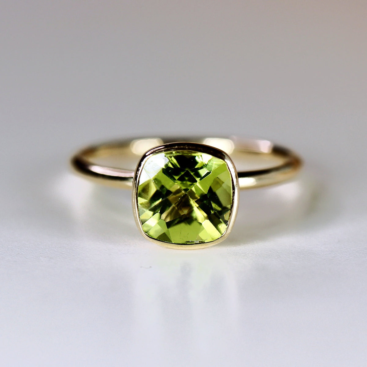 A gold ring with a green peridot gemstone set in a square bezel.