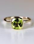 A gold ring with a green peridot gemstone set in a square bezel.