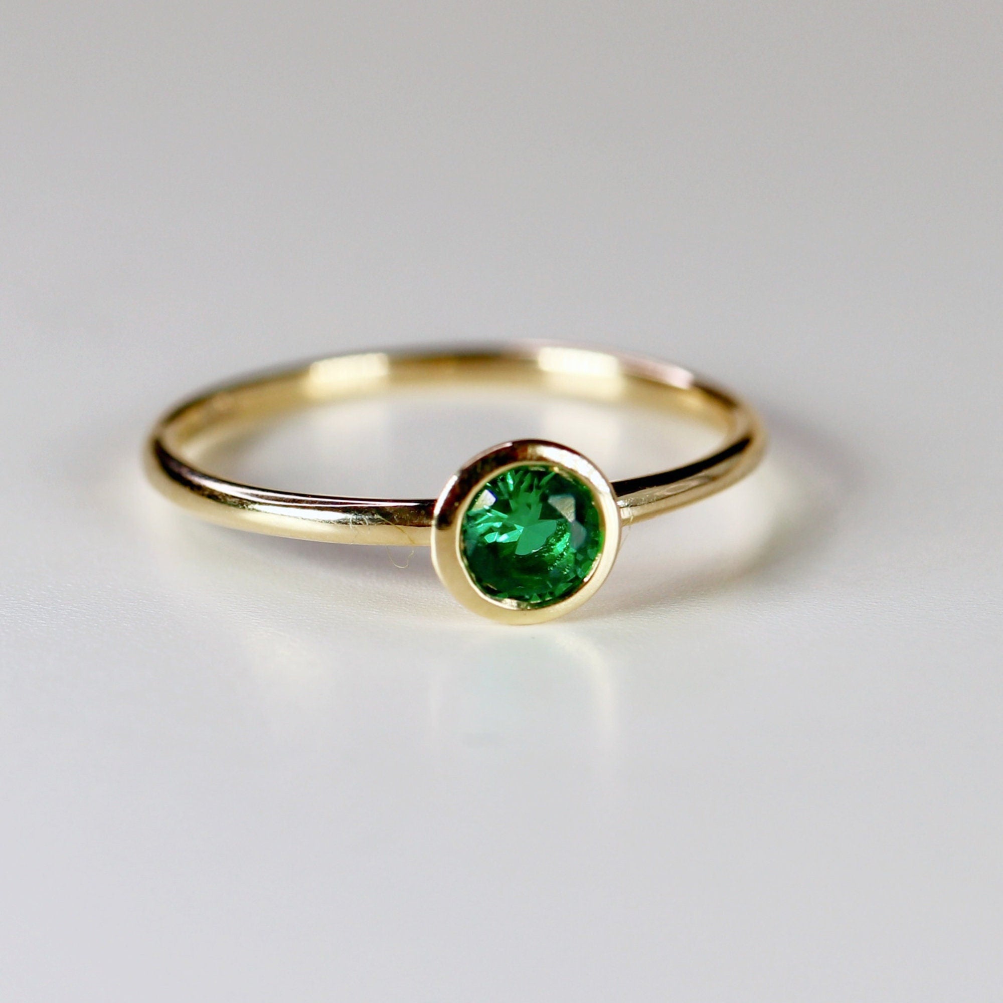 A simple gold band ring with a bezel-set green emerald gemstone.