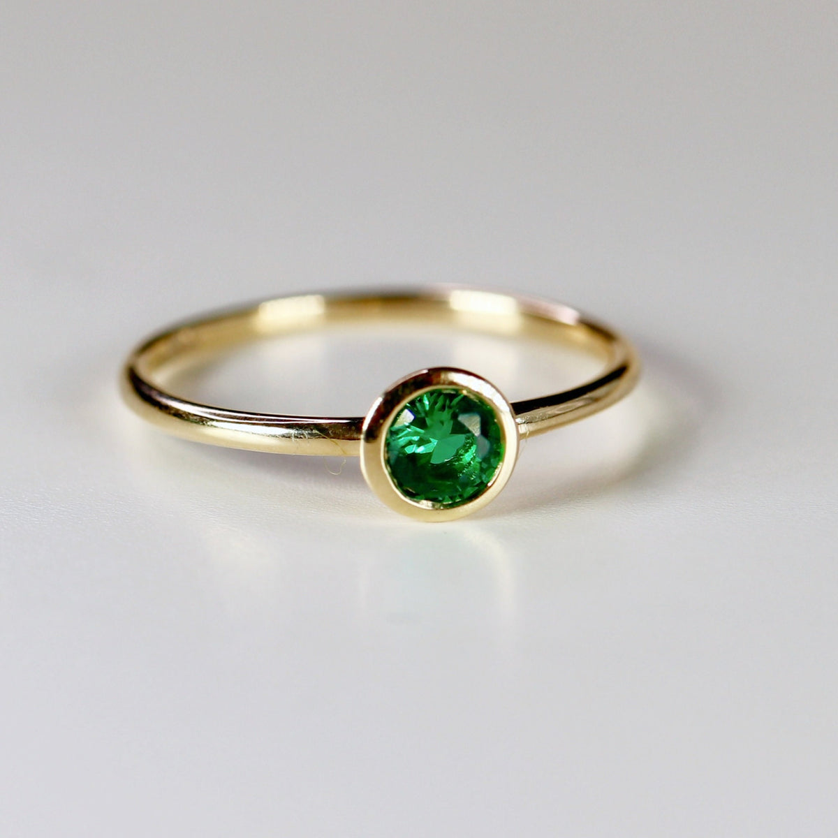 A simple gold band ring with a bezel-set green emerald gemstone.