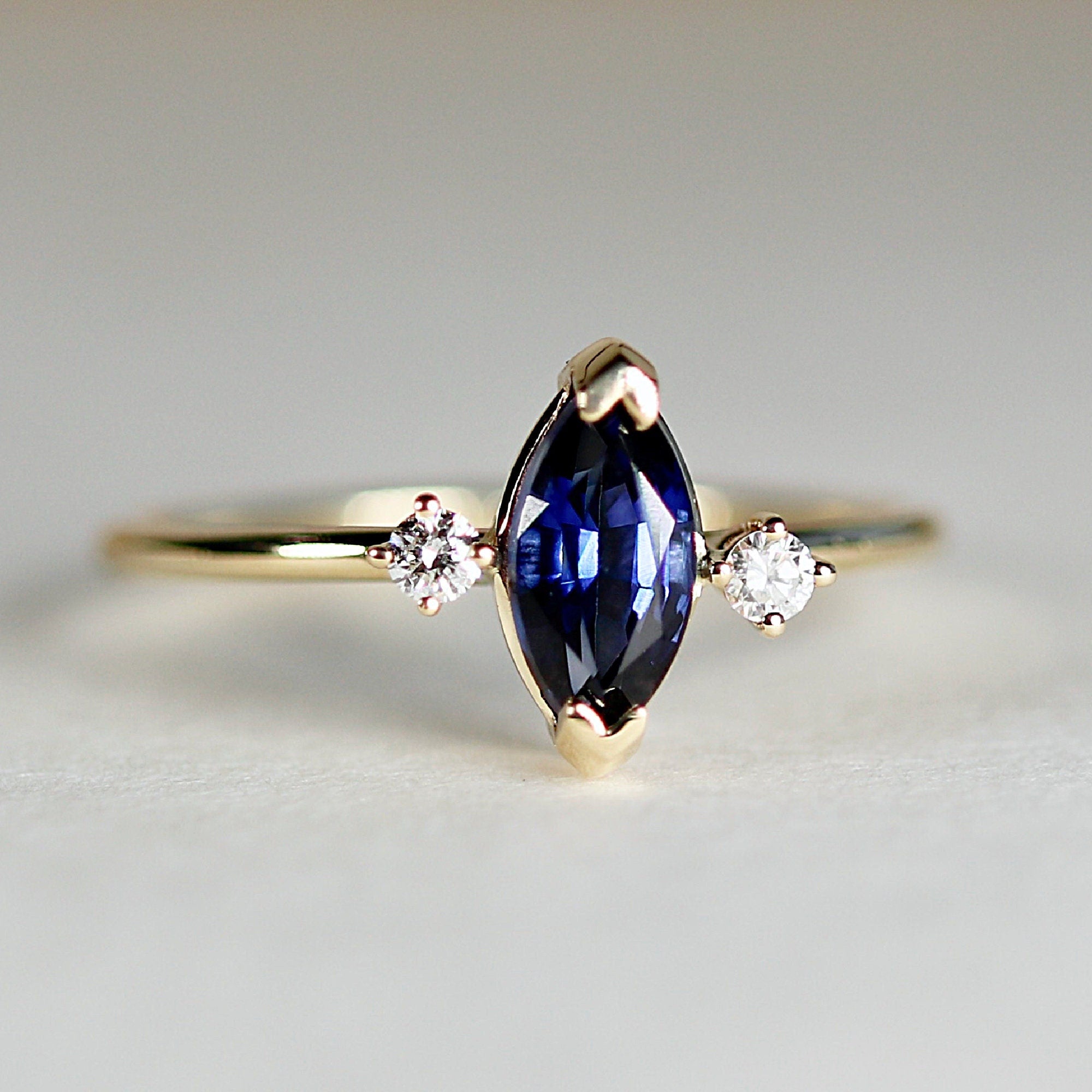 Diamond & Sapphire Engagement Ring A gold ring with a marquise-shaped sapphire gemstone and two smaller round diamonds on either side.