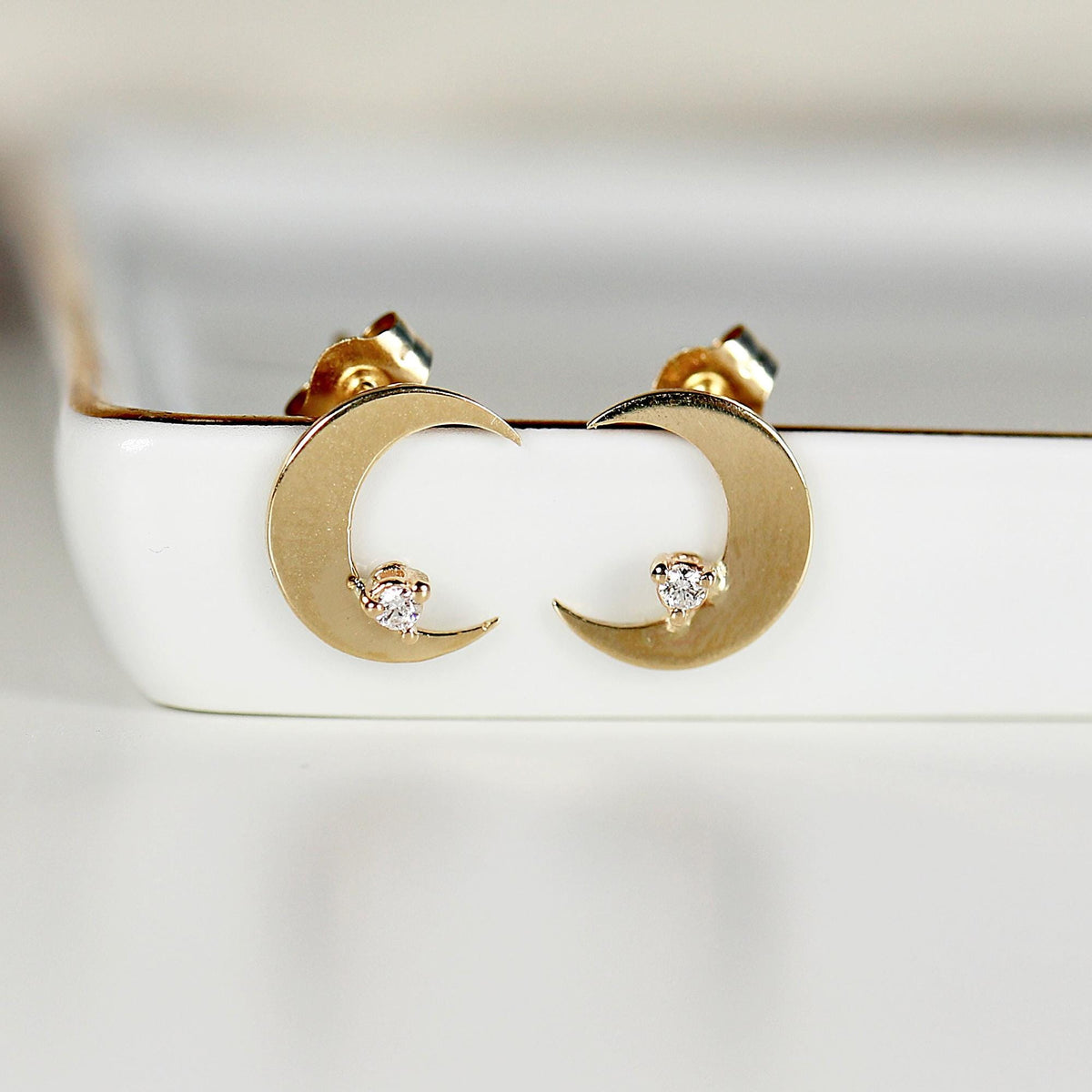A pair of gold crescent moon earrings with a small diamond accent in the center of each moon.