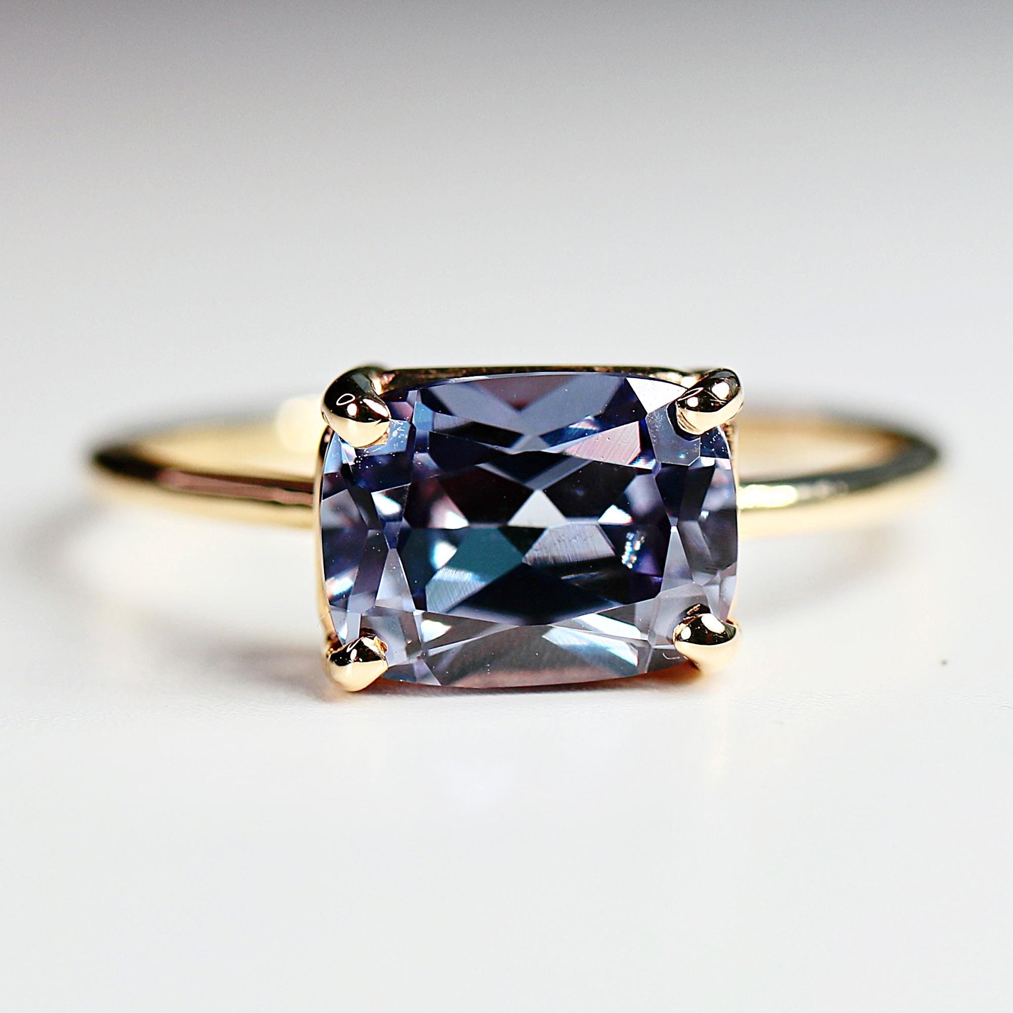 East-west emerald cut lab sapphire solitaire ring in 14k gold, displayed on a white background showing color change effect.