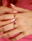 Two gold rings with oval-shaped tourmaline gemstones. The ring on the left has a pink gemstone and the ring on the right has a red gemstone. Both rings have small diamonds set around the gemstones.
