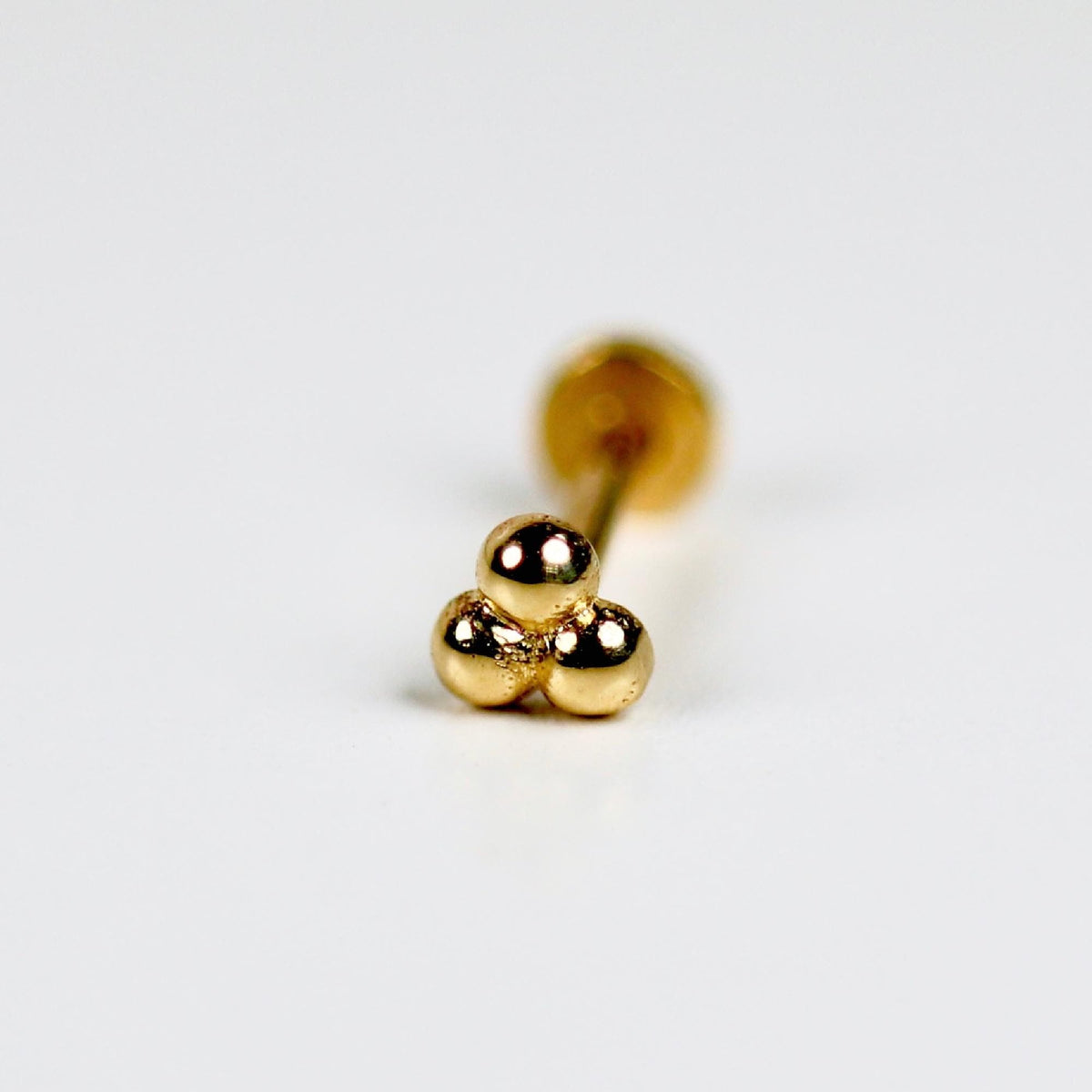 Close-up image of a 14k solid gold trinity flat back earring featuring three small, polished gold balls in a clustered design. The internally threaded post is visible, showing its labret-style backing, suitable for tragus or cartilage piercings. The gold has a warm, smooth finish, and the minimalist design gives a dainty, elegant look