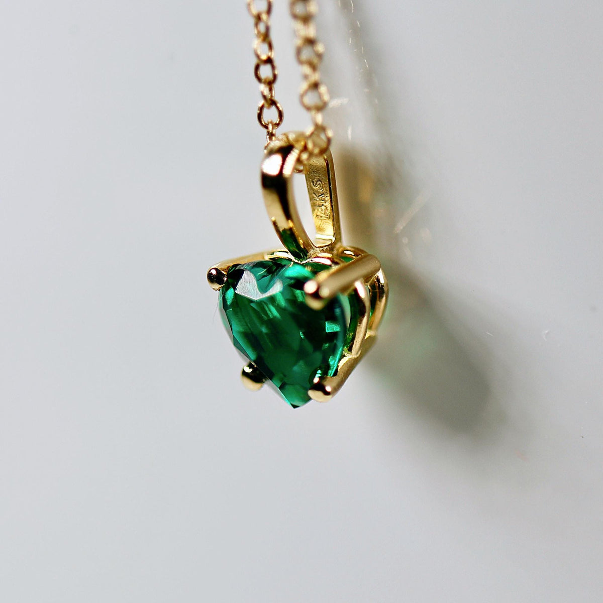 A gold chain necklace with a heart-shaped emerald green emerald pendant.