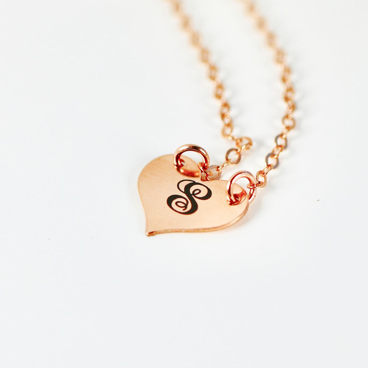 A rose gold necklace with a heart-shaped pendant engraved with the letter "S".