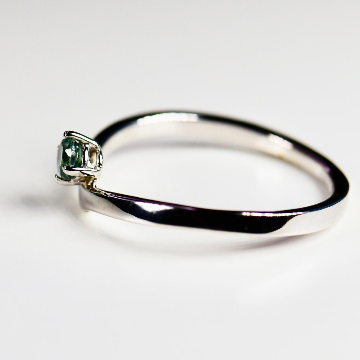 A 14k White gold ring with a single, round, green sapphire gemstone set in the center. The ring is simple and elegant.