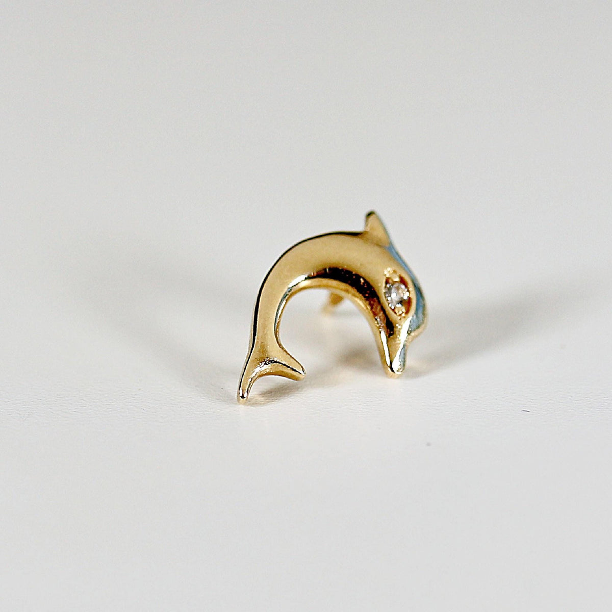 A gold dolphin earring with a single clear diamond for an eye.