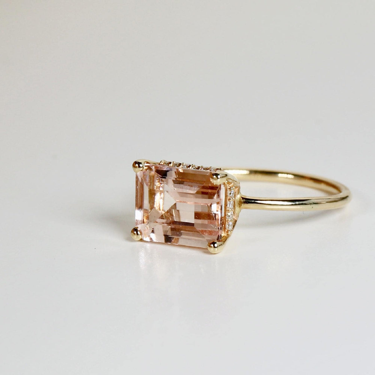 Emerald cut morganite engagement ring with hidden diamond halo in 14k solid gold, blush pink gemstone ring displayed on white background