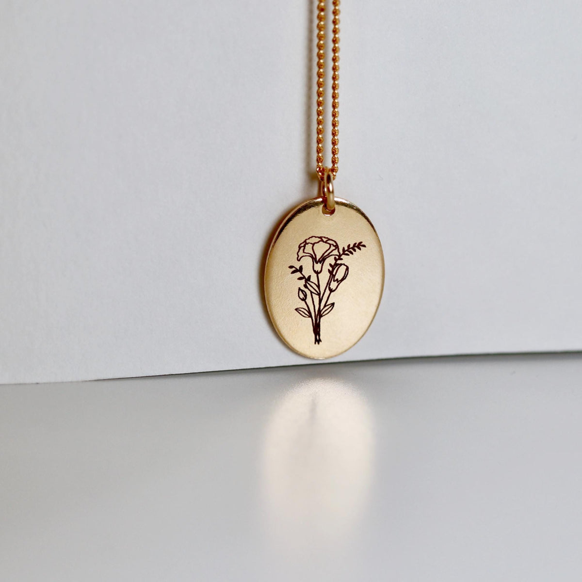 Birth Flower Necklace Gold Filled. A gold chain necklace with a round pendant featuring an engraved floral design. The pendant is oval shaped and has a delicate line drawing of a bouquet of flowers.