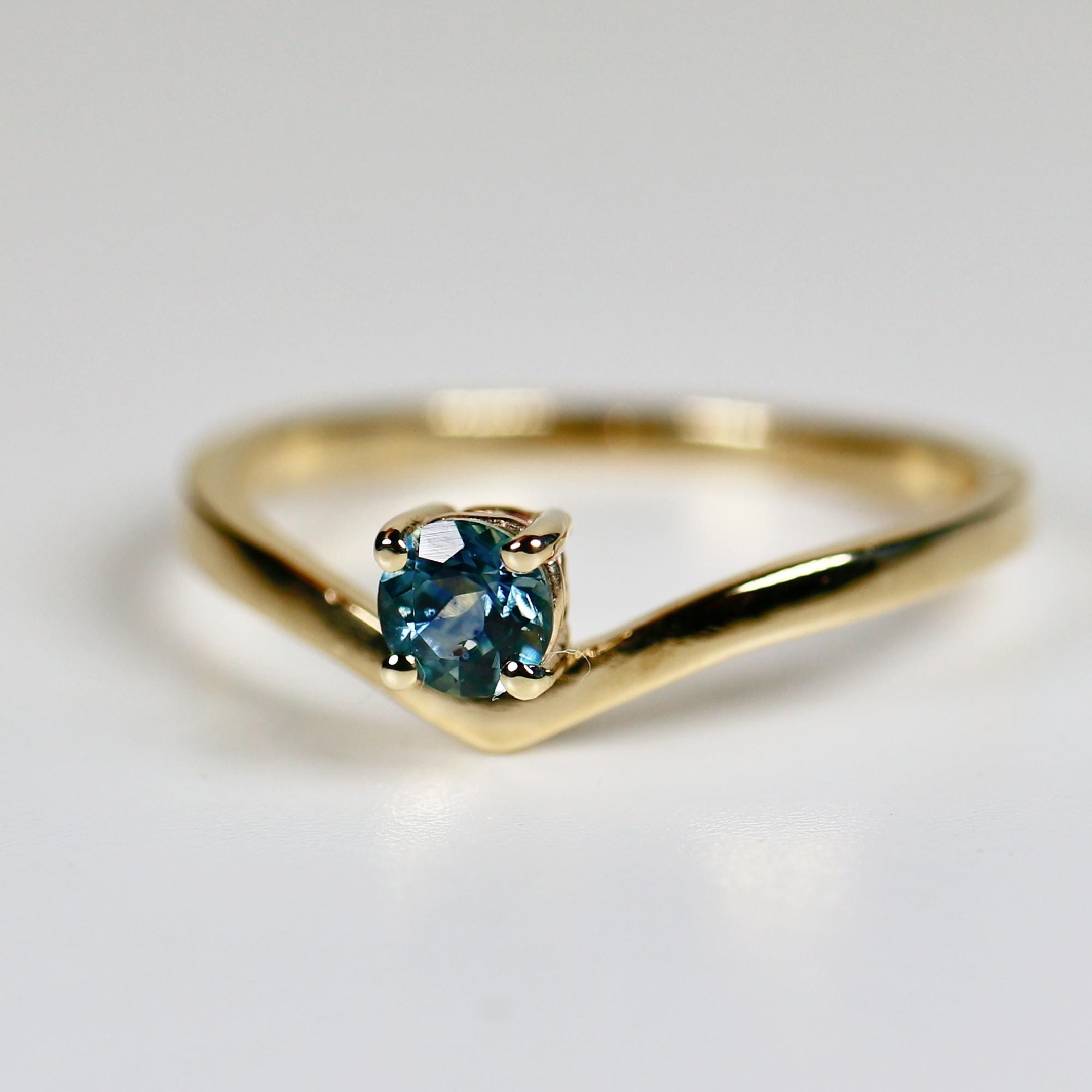 A gold ring with a V-shaped band and a single round blue sapphire gemstone.