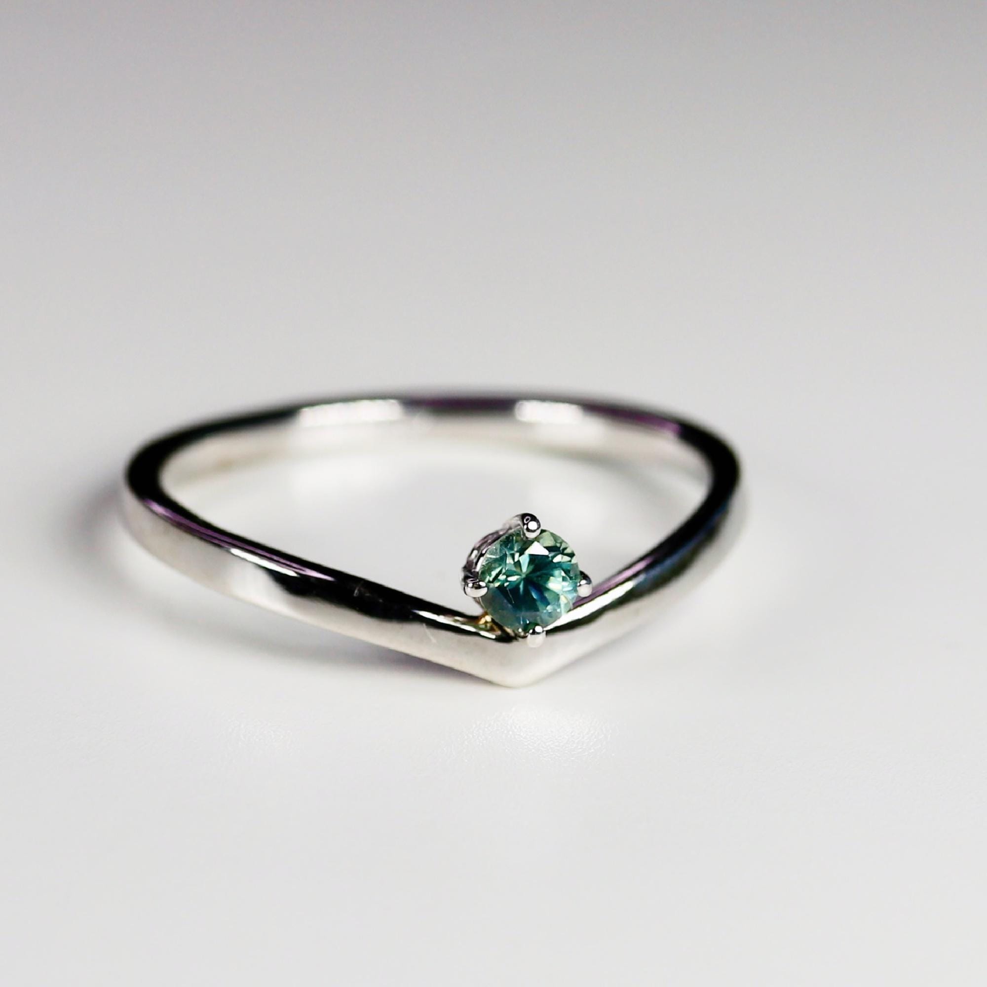 A gold ring with a v-shaped band and a single round green sapphire in the center.