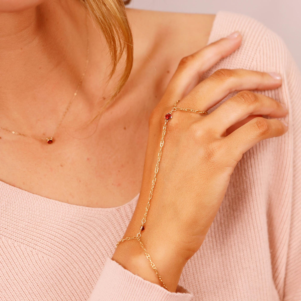 Gold chain bracelet with red garnet gemstone accents. The bracelet is designed to wrap around the wrist and finger.