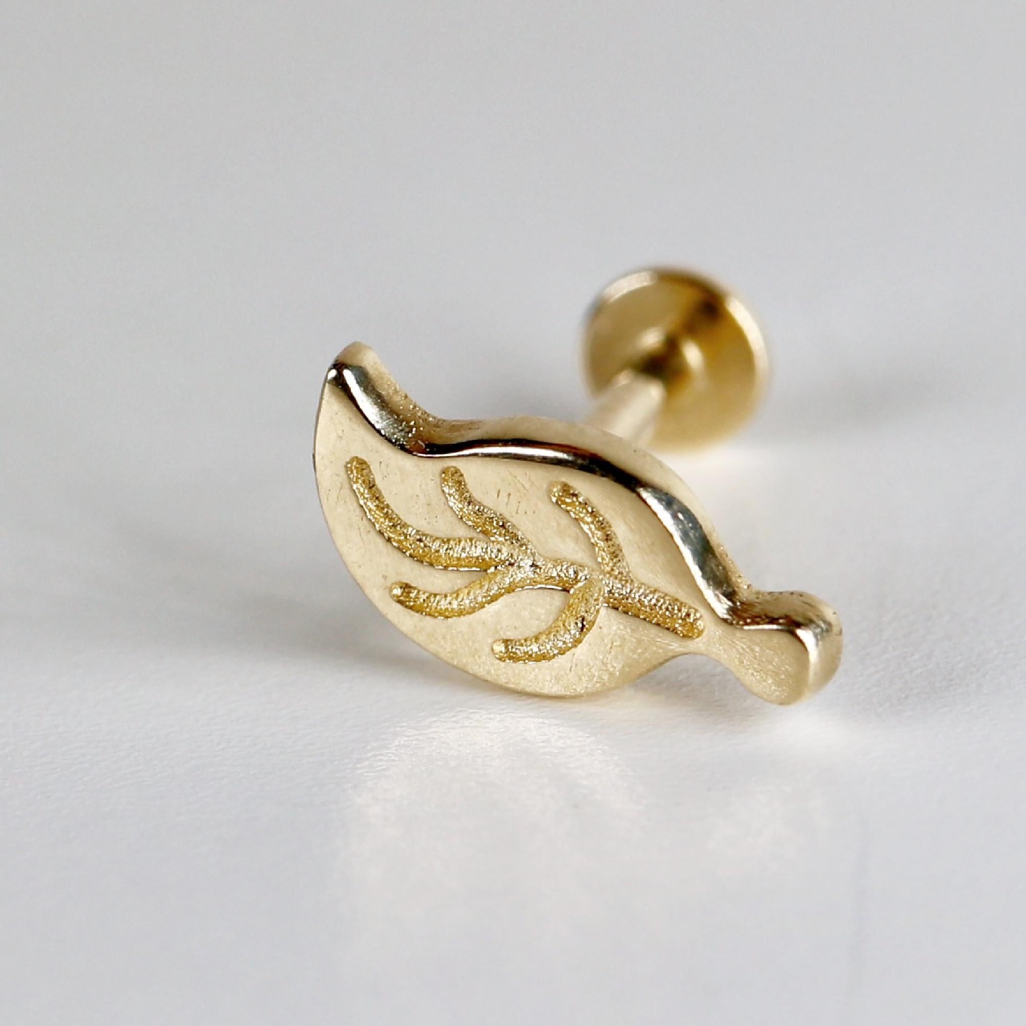Gold leaf-shaped body jewelry with a textured surface. The jewelry is designed for a piercing and has a post with a small ball on the end.