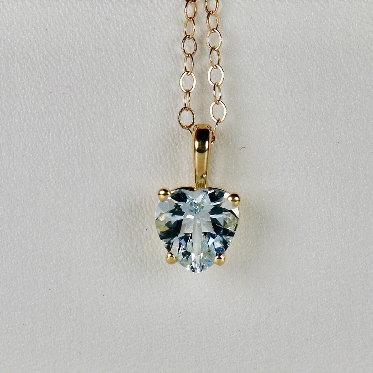 A gold chain necklace with a heart-shaped aquamarine pendant featuring a light blue gemstone.