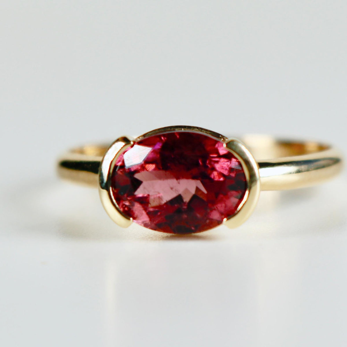 A gold ring with a large oval-shaped pink gemstone set in a bezel setting.