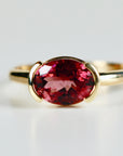 A gold ring with a large oval-shaped pink gemstone set in a bezel setting.