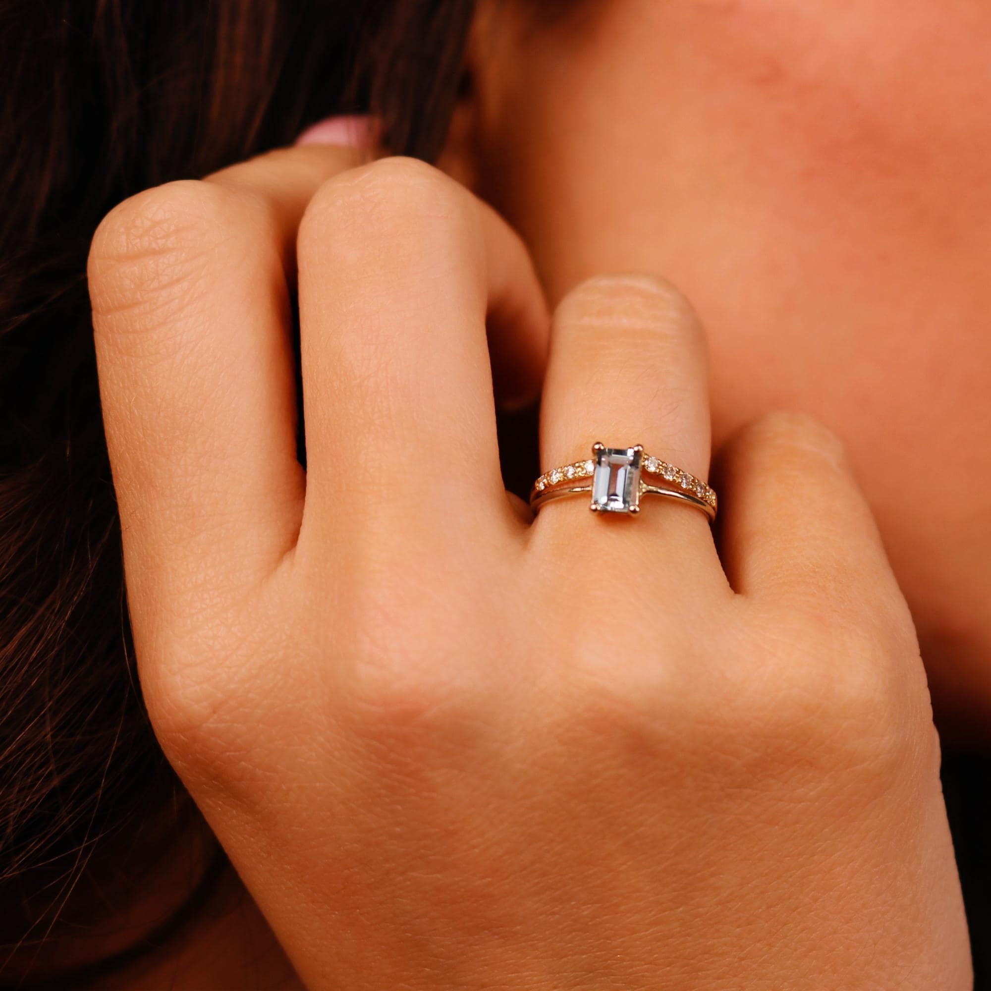 A gold aquamarine ring with a single, rectangular, light blue gemstone surrounded by smaller, clear gemstones.