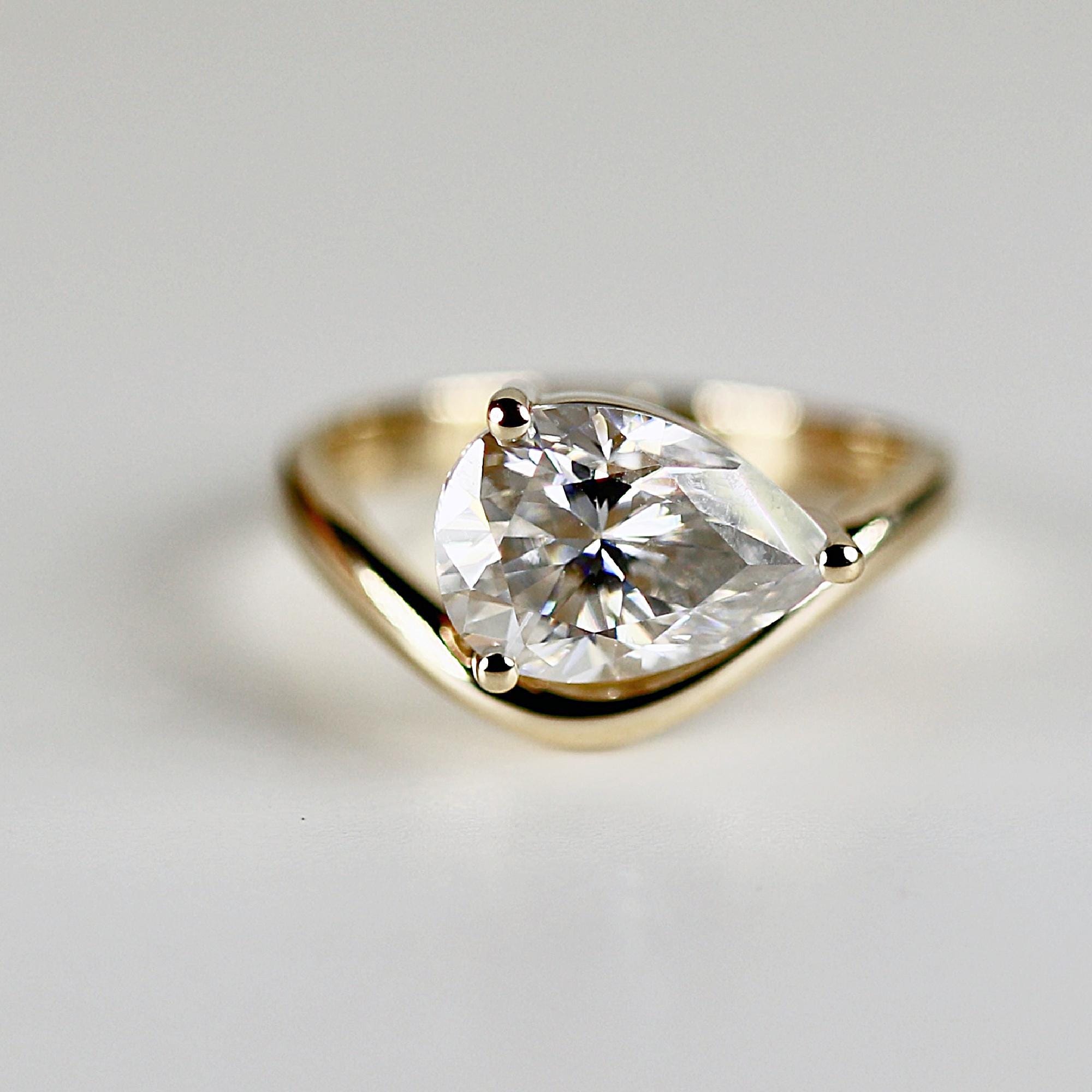A 2 carat pear-cut moissanite ring set in 14k solid gold with a unique east-west floating design. Elegant anniversary or engagement gift for her.