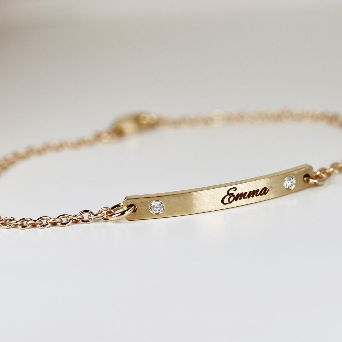 A gold bracelet with a delicate chain and a rectangular bar. The bar is engraved with the name &amp;quot;Emma&amp;quot; and features two small, sparkling gemstones. The bracelet is designed for everyday wear.