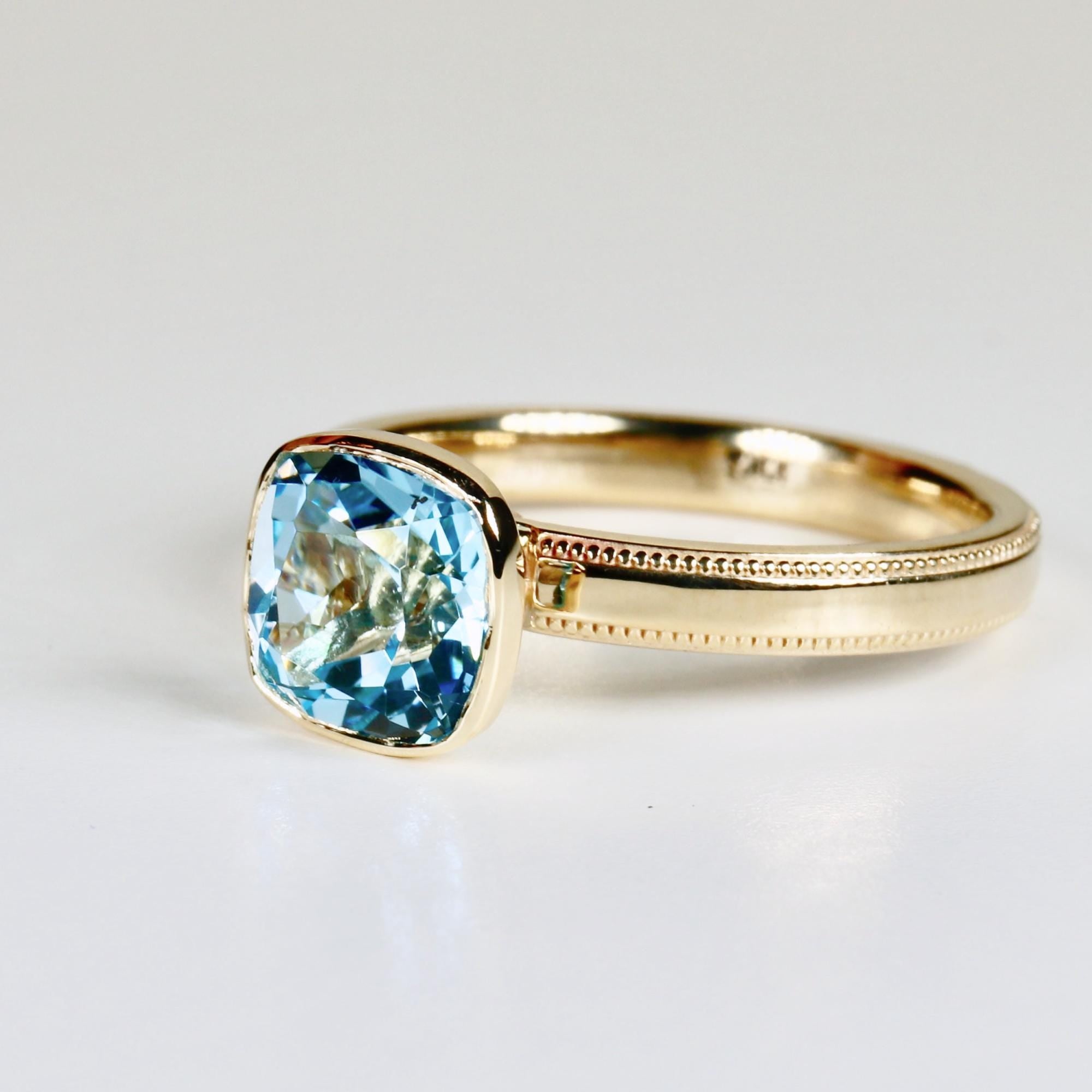 Cushion cut blue topaz solitaire ring set in 10k gold with a bezel setting, photographed on a clean white background.