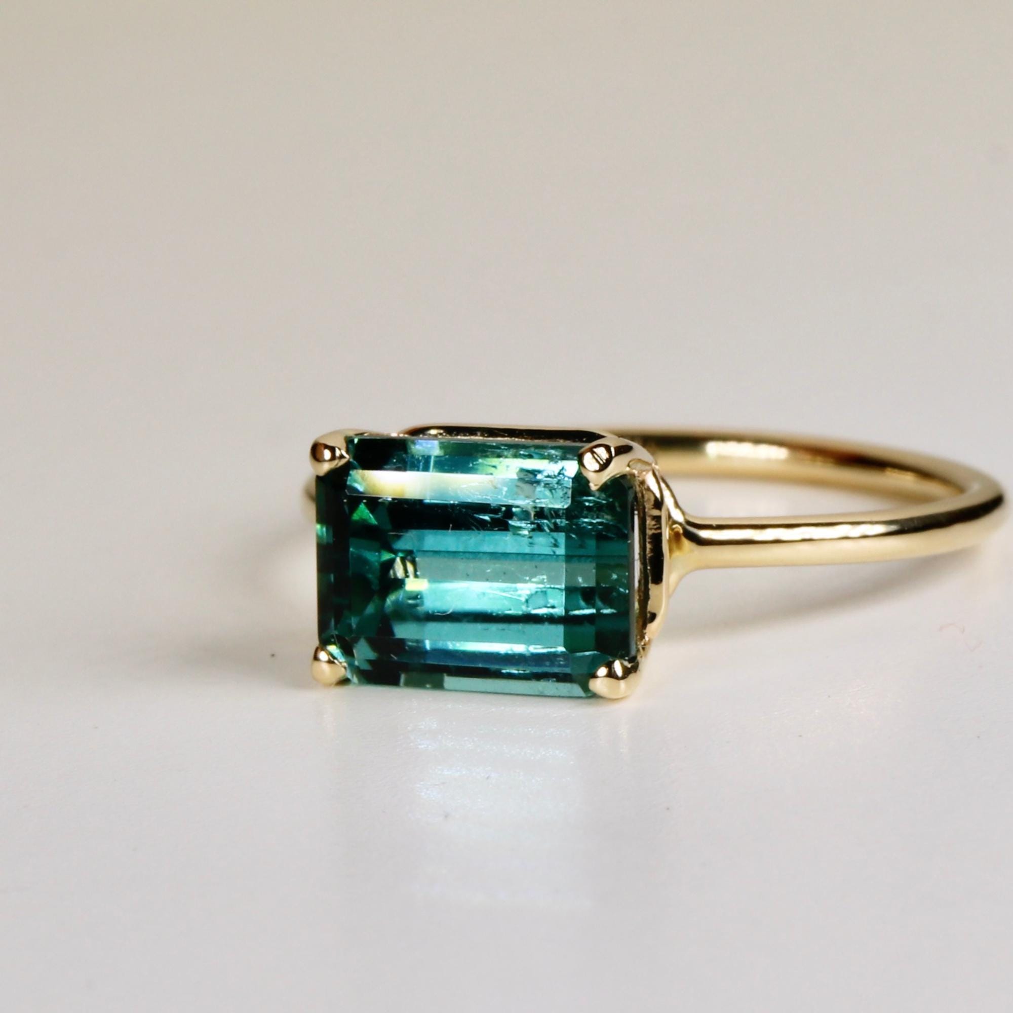 Emerald cut green tourmaline ring set east-west in 14k gold, displayed on a white background as a bold gemstone statement ring.