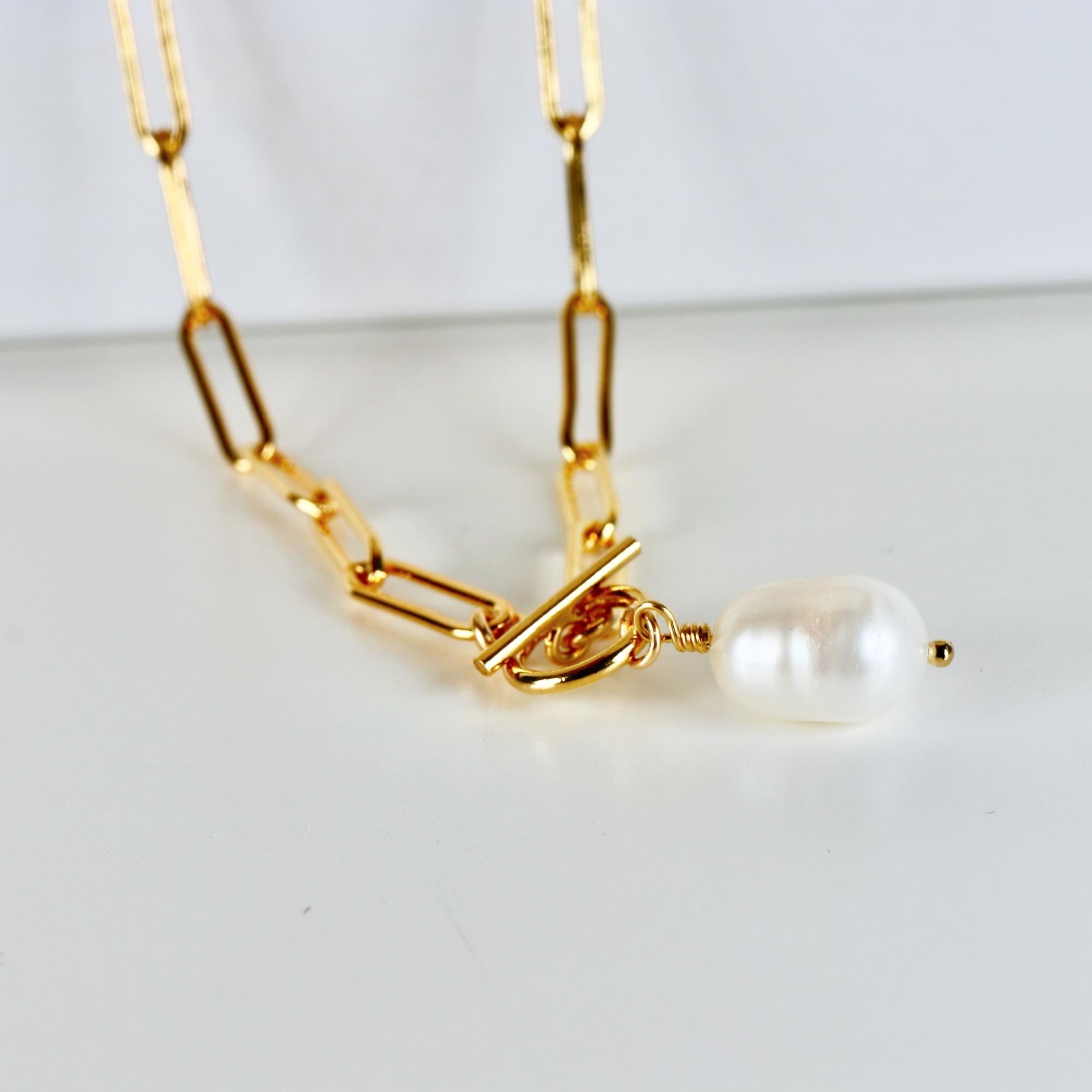Close-up of a natural baroque pearl pendant hanging from a gold-filled paperclip chain with a toggle clasp, displayed on a white background.