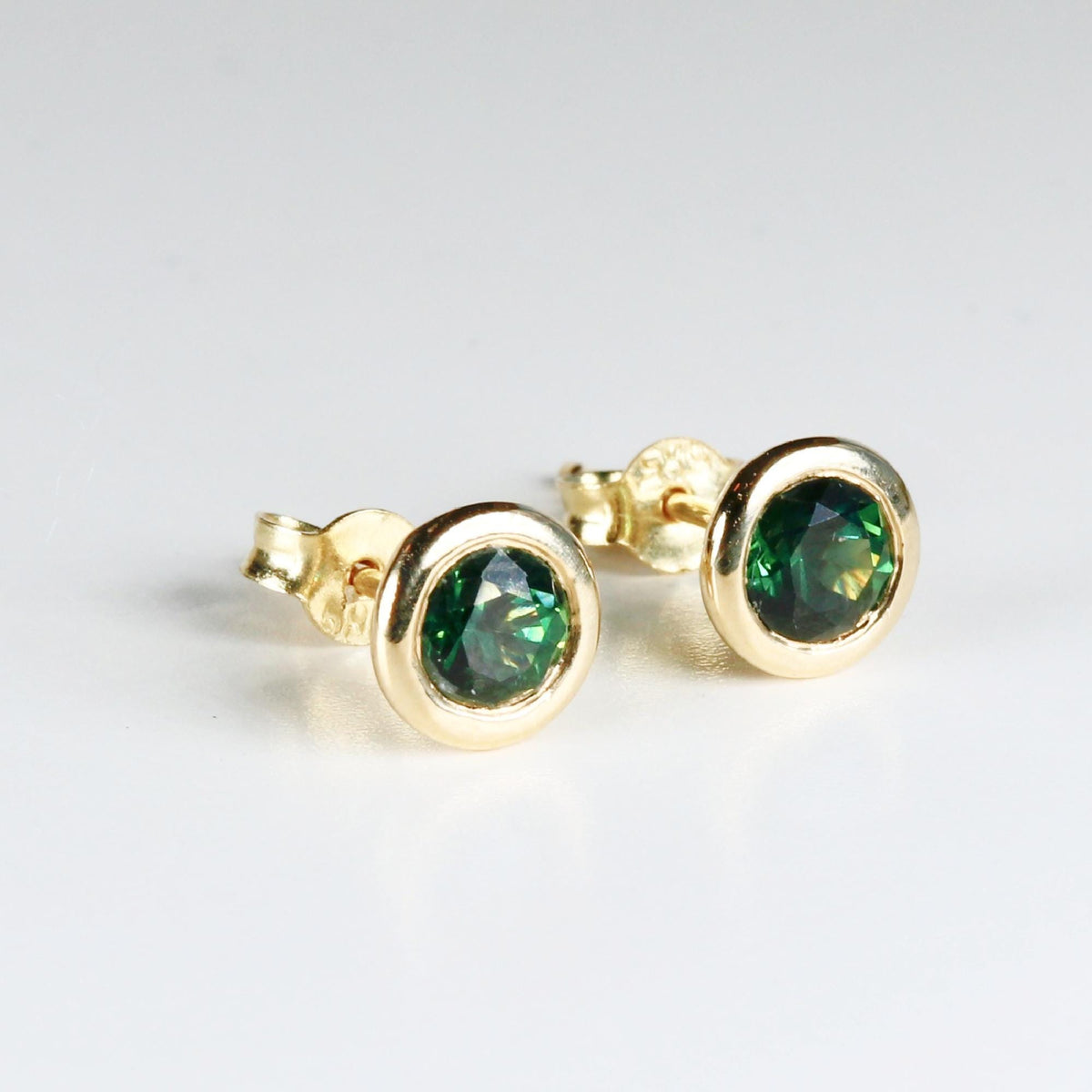 Pair of green sapphire martini bezel stud earrings in 14k solid gold, displayed on a clean white background.