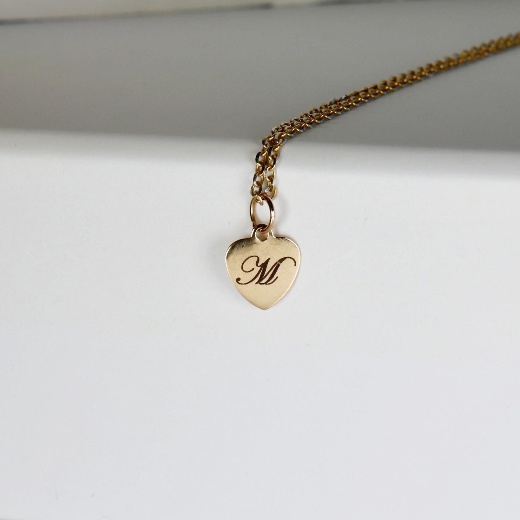 Gold filled heart pendant necklace engraved with a single initial, shown on a woman’s neck. Dainty chain with a polished heart charm.