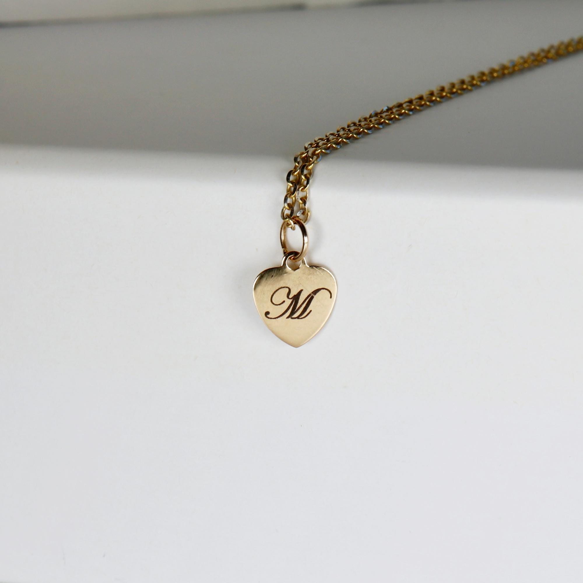 Gold filled heart pendant necklace engraved with a single initial, shown on a woman’s neck. Dainty chain with a polished heart charm.