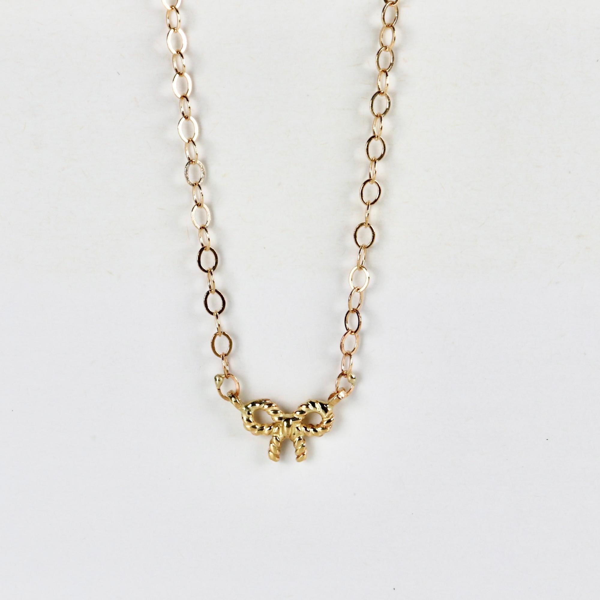 Tiny 14k solid gold bow necklace with twisted ribbon design, displayed on a white background.