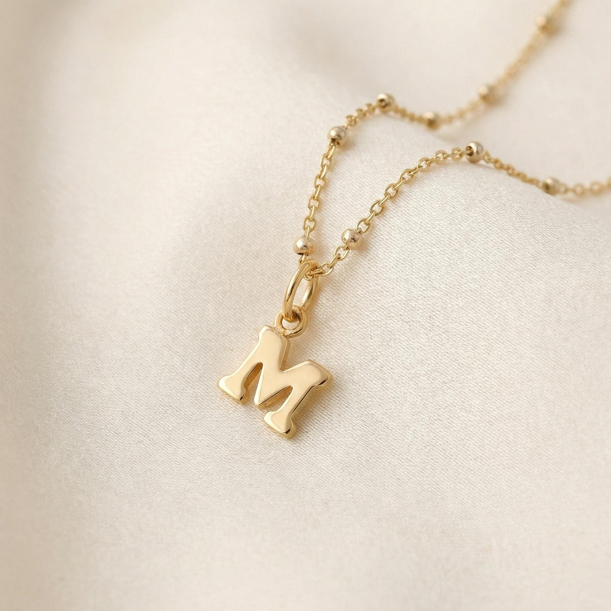 Gold filled satellite chain necklace with a small letter pendant on a white background.