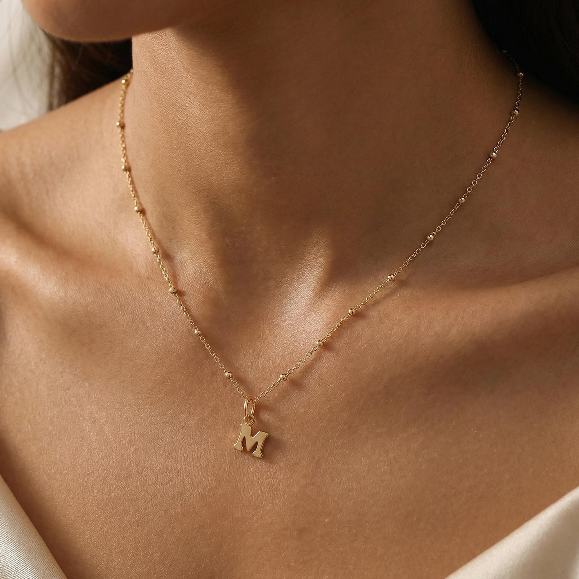 Woman wearing a dainty gold initial necklace with bead chain