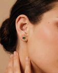 Green emerald heart earrings in solid gold, dainty gemstone studs for everyday wear, worn on ear.