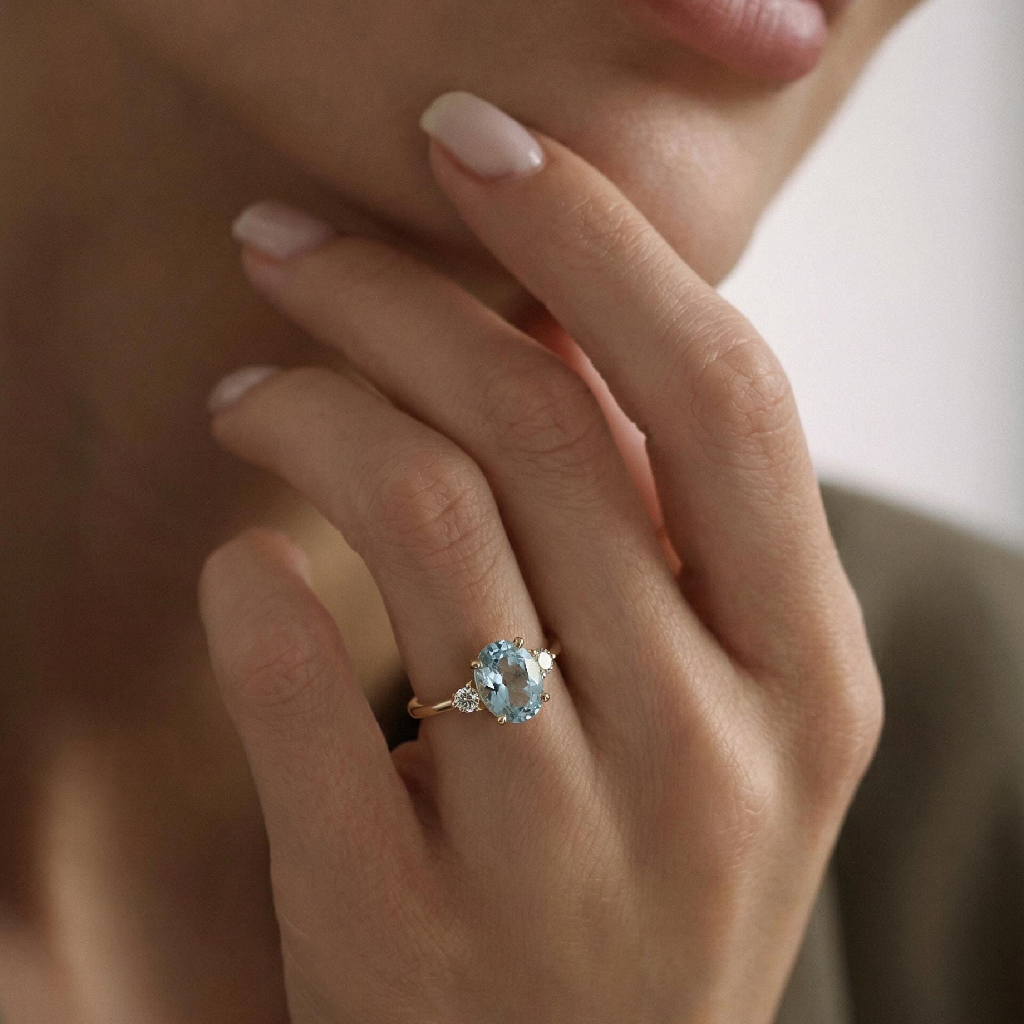Prong set oval aquamarine engagement ring on model hand in 14k gold